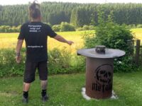 Partypalme zeigt auf eine Feuertonne mit Feuerplatte